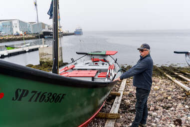 Man standing on a green fishing boat on a stone beach